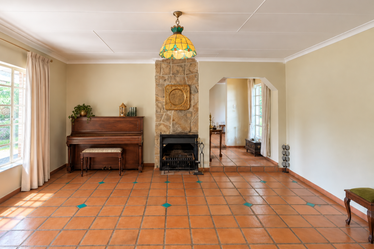 Spacious living room featuring terracotta tile flooring, a central stone fireplace, and a decorative pendant light, leading into an adjacent room through an archway.