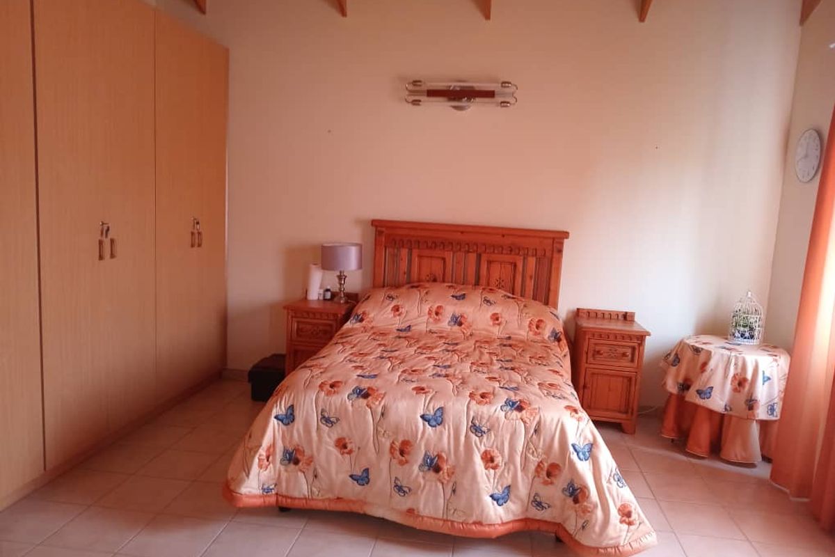 A spacious bedroom featuring built-in wooden wardrobes, tiled flooring, and exposed timber ceiling beams.