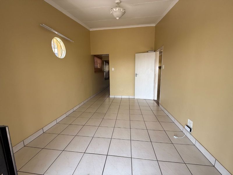 An empty living area featuring neutral wall paint, ceramic floor tiles, and a unique porthole window, offering a blank canvas for interior design.