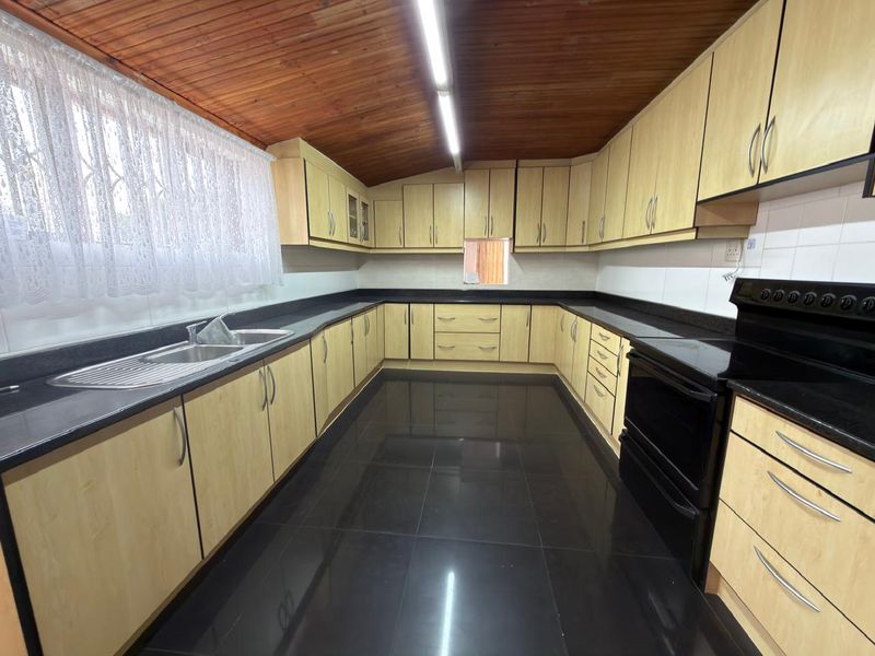 Spacious kitchen featuring light wood cabinetry, dark granite countertops, black tiled flooring, and a distinctive timber tongue and groove ceiling.