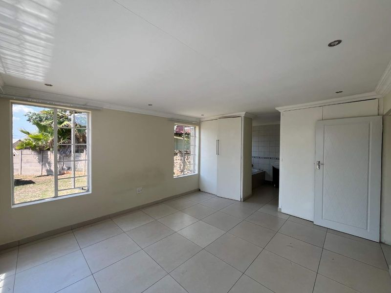 A spacious, empty bedroom featuring neutral tiled flooring, built-in cupboards, and recessed lighting, with direct access to an en-suite bathroom area.