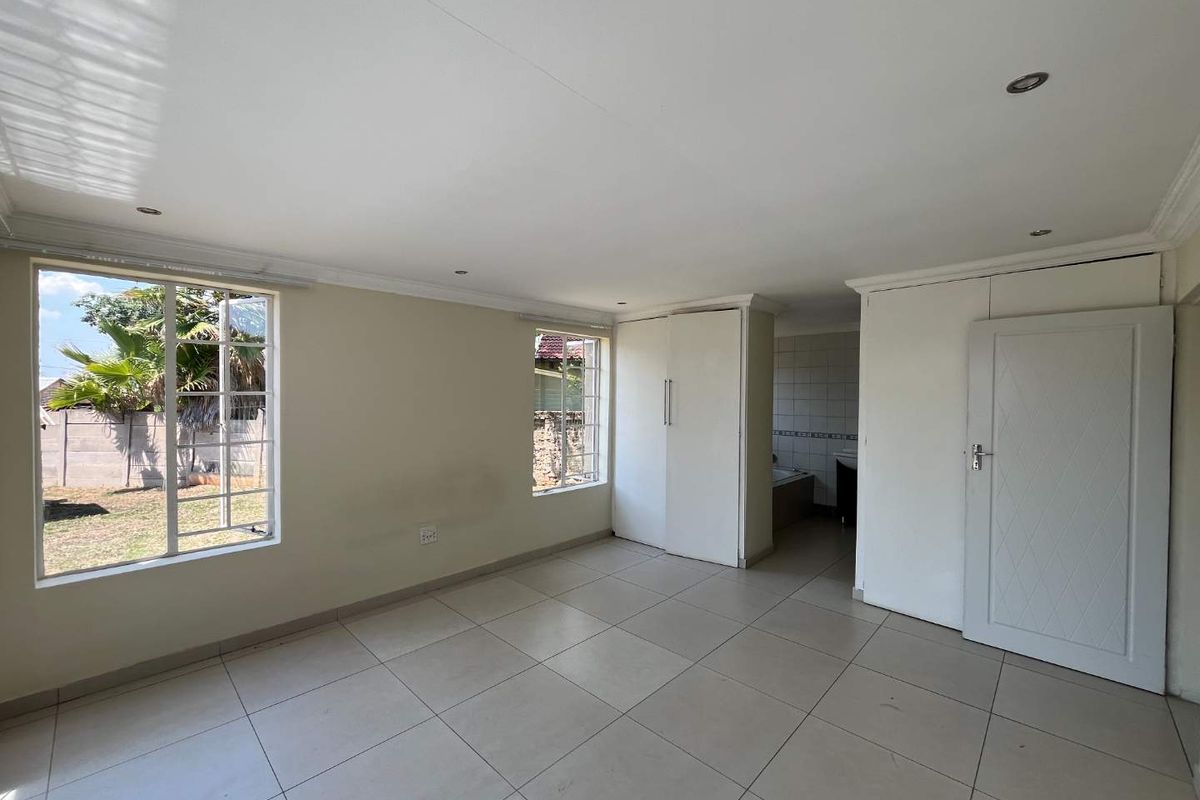 A spacious, empty bedroom featuring neutral tiled flooring, built-in cupboards, and recessed lighting, with direct access to an en-suite bathroom area.