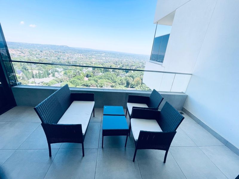 A modern balcony featuring a sleek glass balustrade and large format floor tiles, offering expansive elevated views of the surrounding landscape.