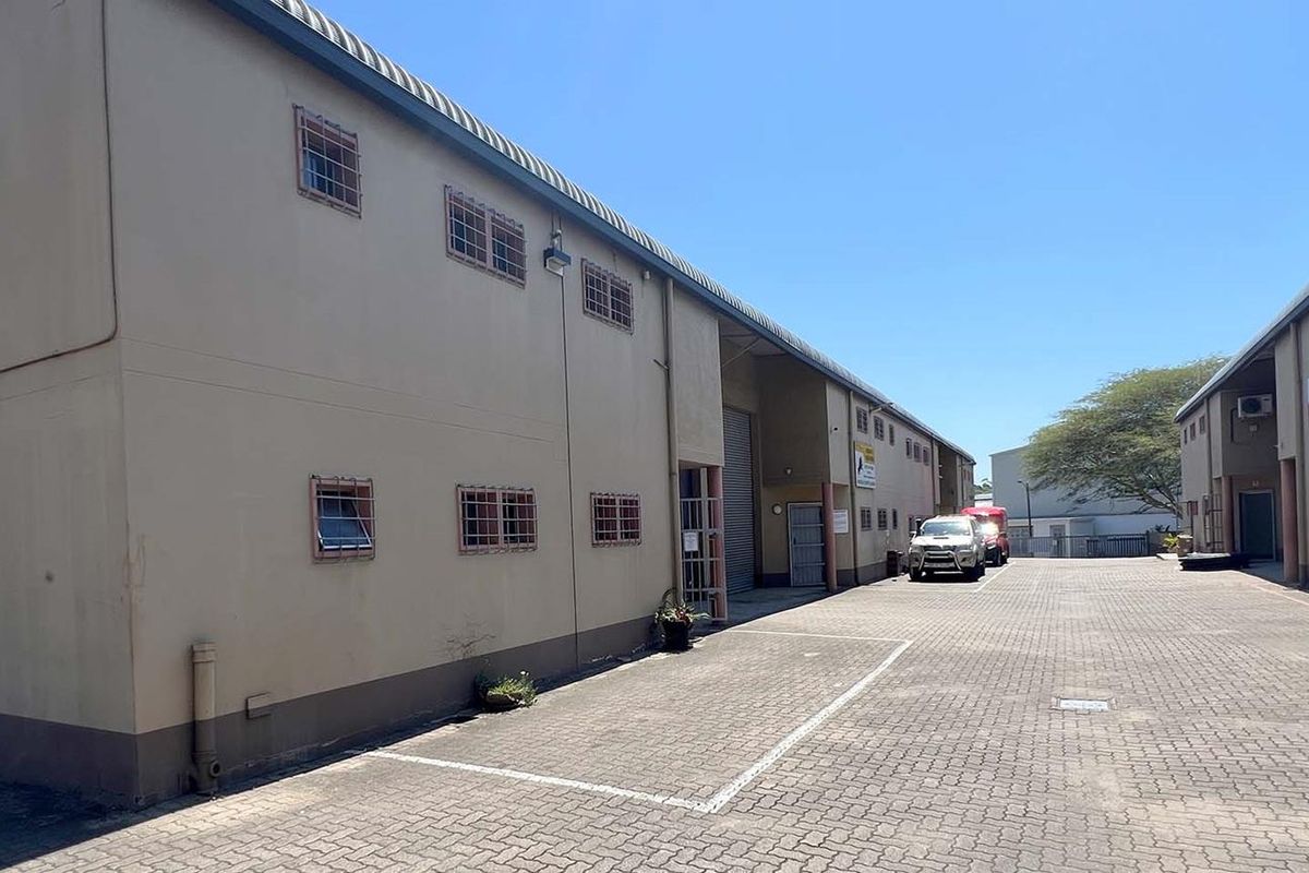 Exterior view of an industrial complex featuring paved yard space, multi-level warehouse units, security bars on windows, and external air conditioning units.