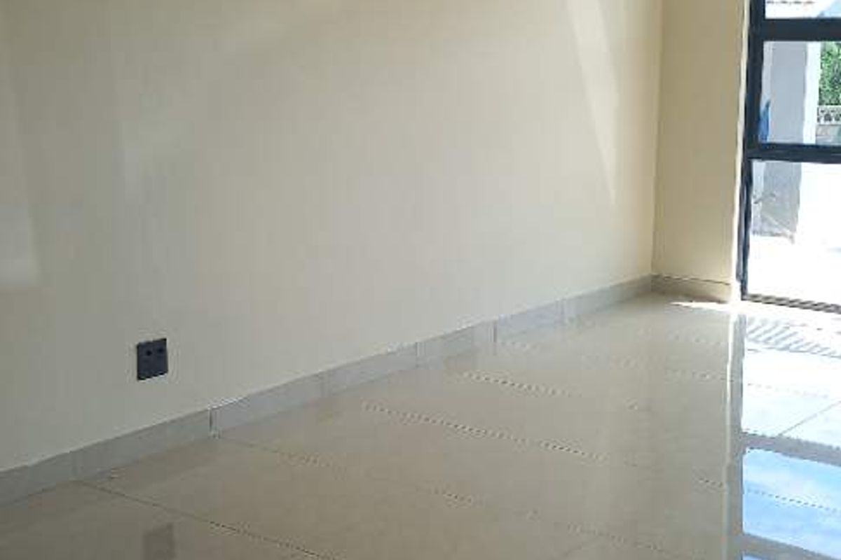 A bright, empty living area featuring neutral painted walls and polished porcelain floor tiles, with a large window providing natural light.