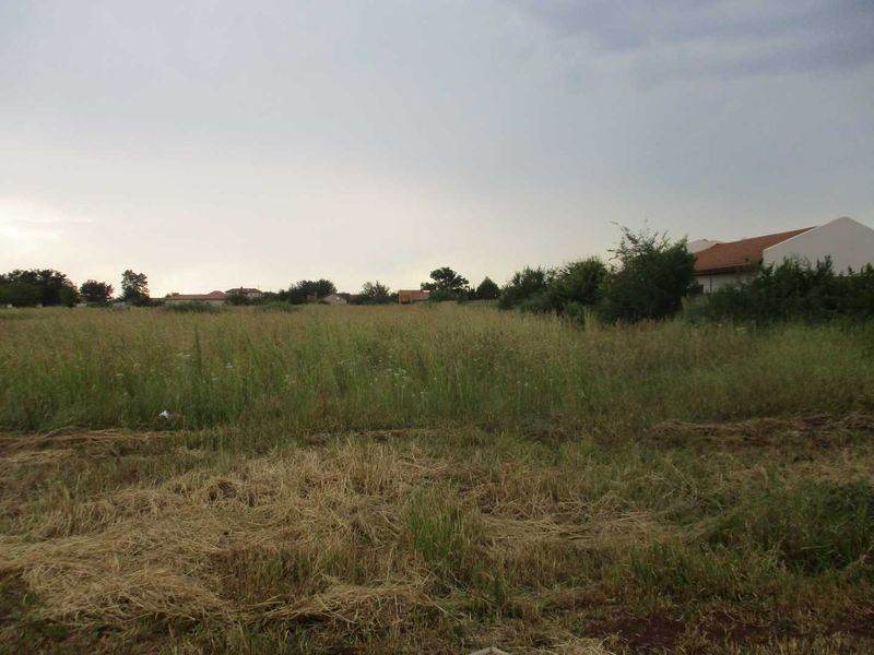 A view of a vacant residential plot of land with natural grass cover, suitable for future development.