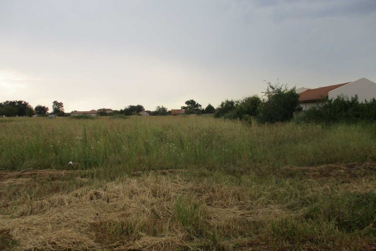 A view of a vacant residential plot of land with natural grass cover, suitable for future development.