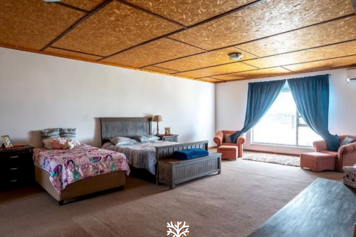 Spacious bedroom featuring a unique OSB panel ceiling, neutral wall finishes, and large windows with views, providing a comfortable and functional living space.