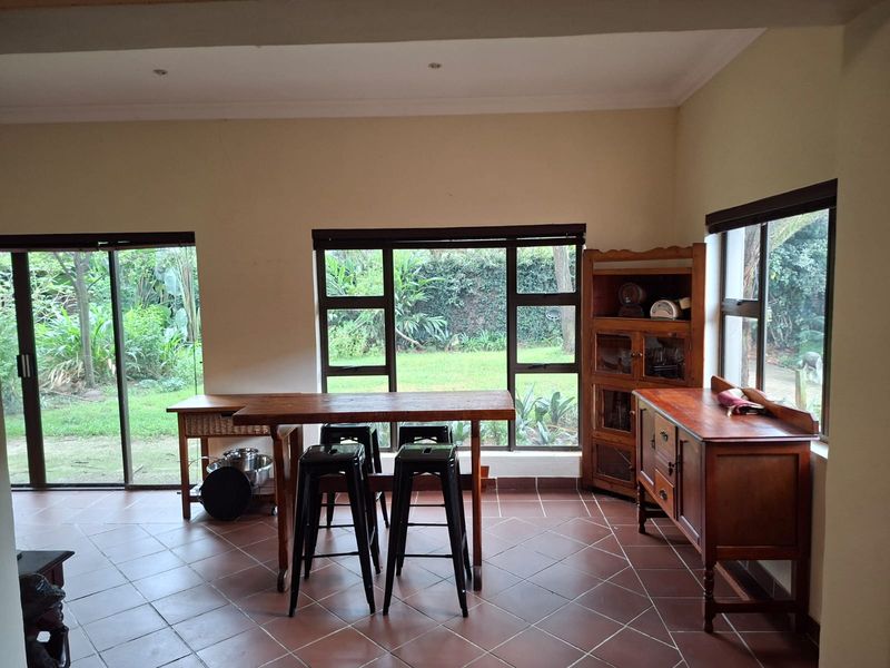 A bright living area featuring terracotta-style floor tiles, large windows, and sliding glass doors that provide ample natural light and views of the garden.