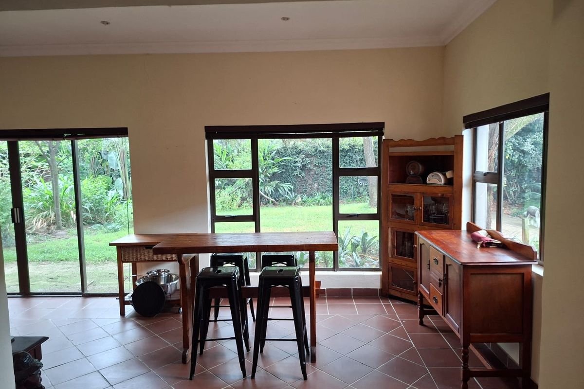 A bright living area featuring terracotta-style floor tiles, large windows, and sliding glass doors that provide ample natural light and views of the garden.