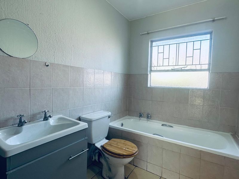 A functional bathroom featuring a vanity basin, toilet, and bathtub with tiled walls and flooring, offering a blank canvas for modernization.