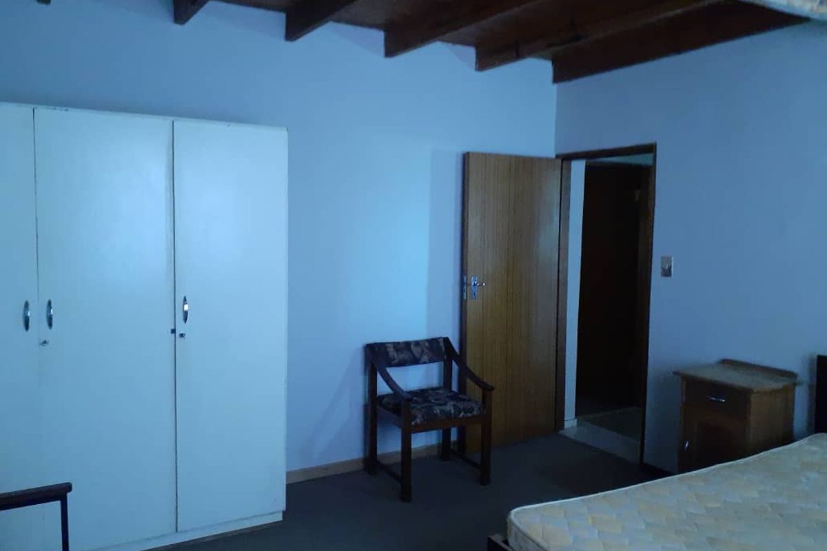 A bedroom featuring exposed timber ceiling beams, built-in wardrobe cabinetry, and a standard wooden door leading to an adjacent hallway.