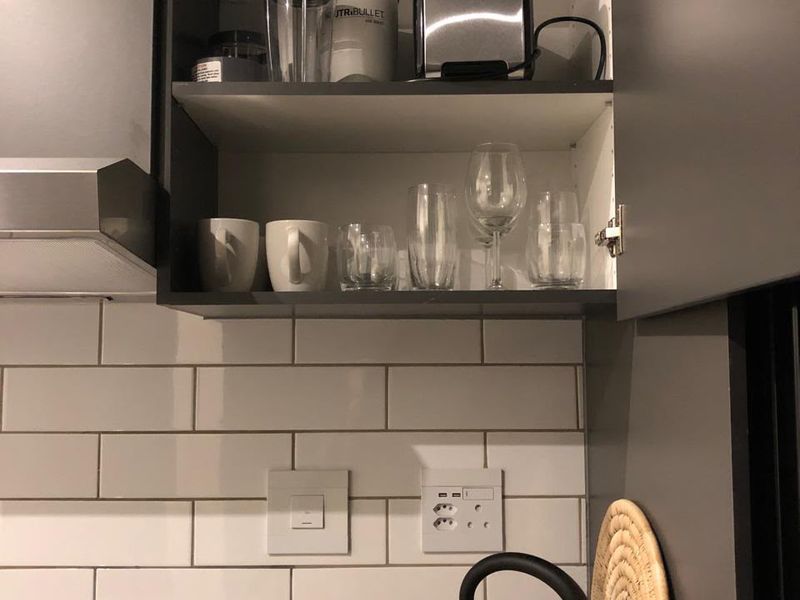 A modern kitchen featuring grey cabinetry, a white subway tile backsplash, and stone countertops with integrated electrical outlets and an extractor fan.
