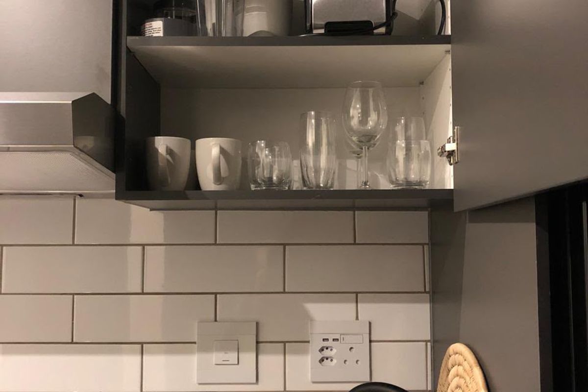 A modern kitchen featuring grey cabinetry, a white subway tile backsplash, and stone countertops with integrated electrical outlets and an extractor fan.