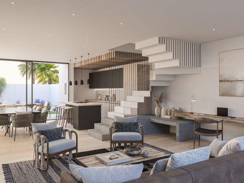 Modern open-plan living area featuring a sleek kitchen, integrated staircase, built-in desk, and seamless flow to the outdoor patio through large sliding glass doors.