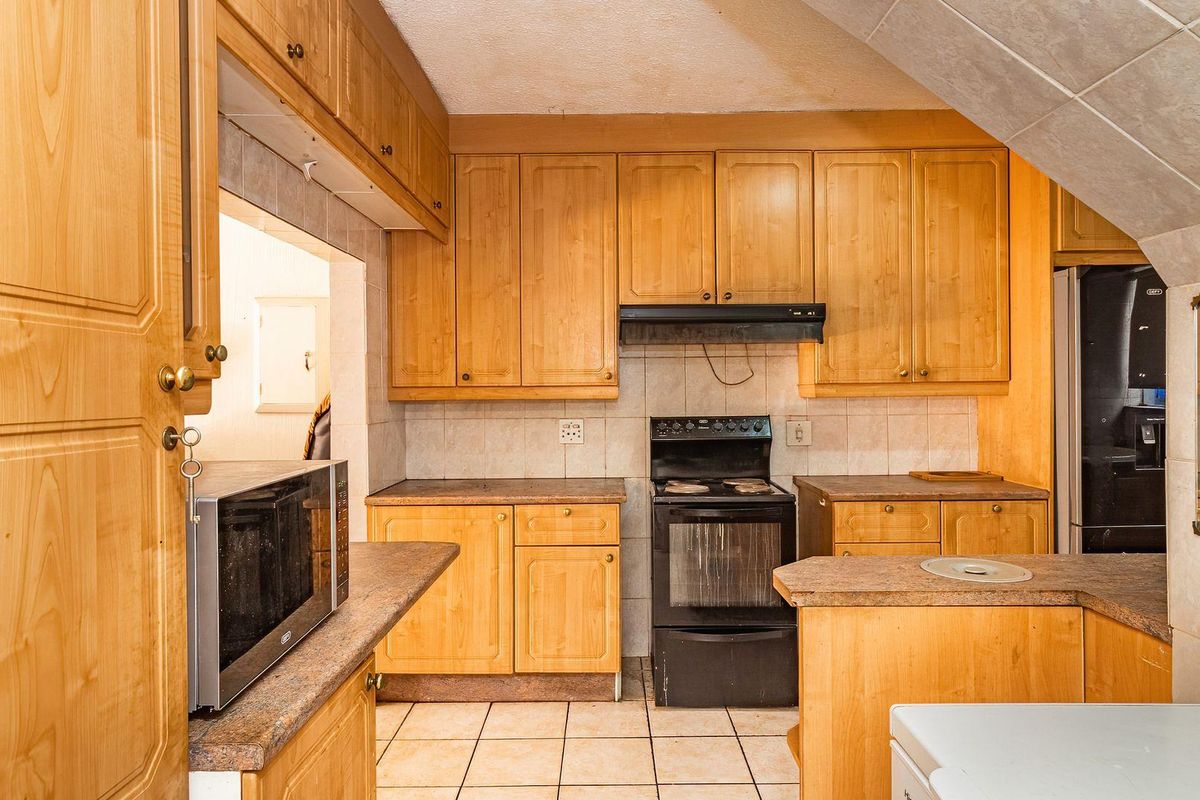 A dated kitchen featuring wooden cabinetry, laminate countertops, tiled backsplash, and a freestanding oven with an extractor fan.