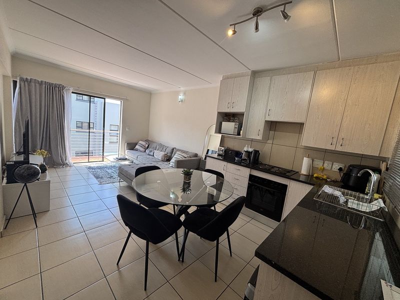 Open-plan living area featuring a modern kitchen with granite countertops, built-in oven, and tiled flooring, leading to a balcony through sliding doors.