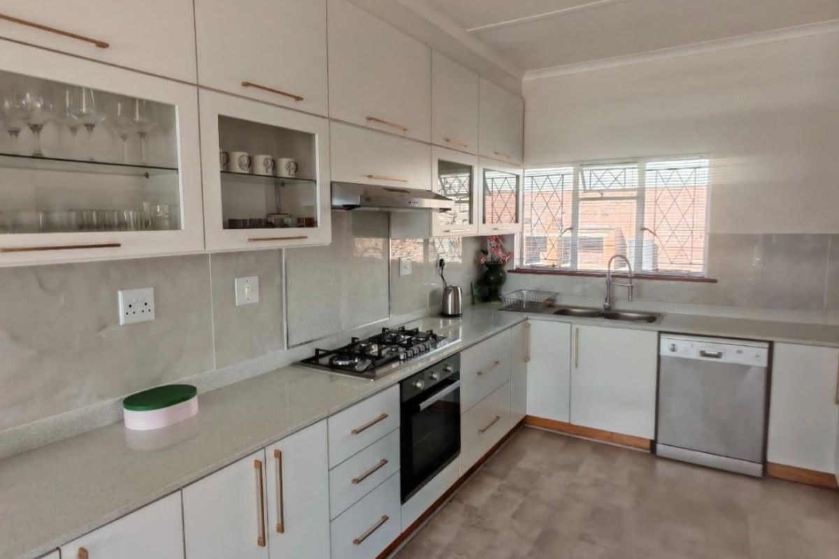 A well-maintained kitchen featuring white cabinetry, stone countertops, a gas hob, built-in oven, extractor fan, and integrated dishwasher with ample storage space.