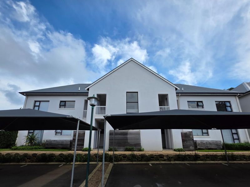 Front elevation of a modern apartment complex featuring covered parking bays, paved driveway, and well-maintained building facade with aluminium window frames.