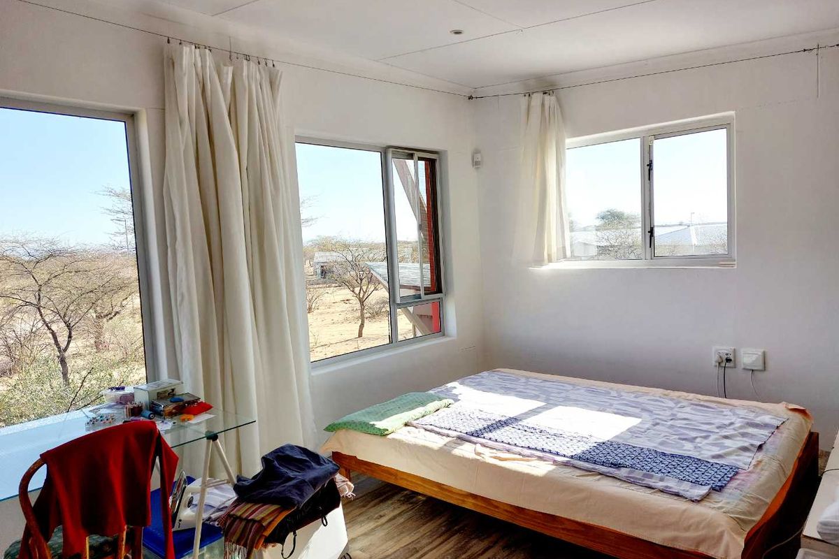 A bright bedroom featuring large windows with natural light, wood-look flooring, and recessed ceiling lighting, offering views of the surrounding landscape.