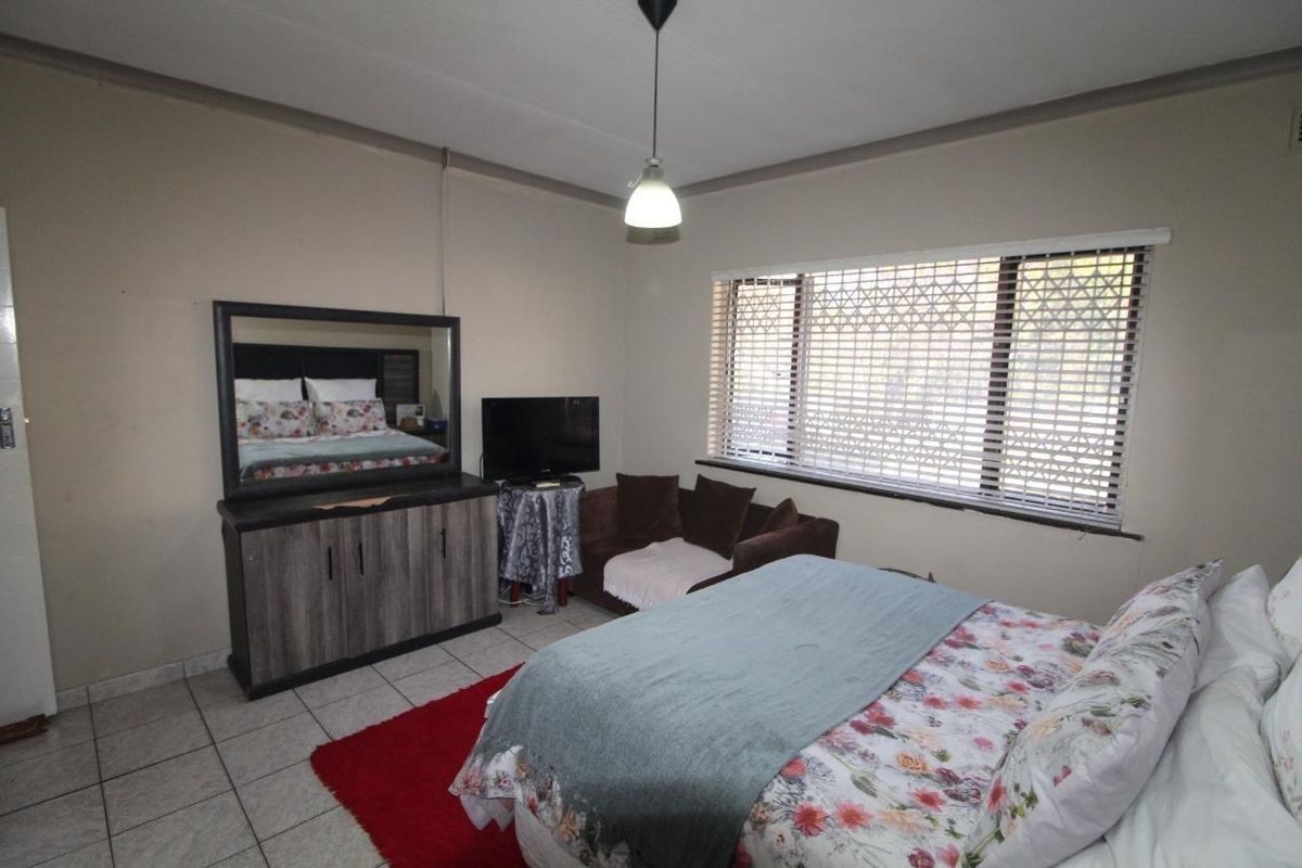 A bedroom featuring tiled flooring, a large window with a security gate, and a central pendant light fixture.