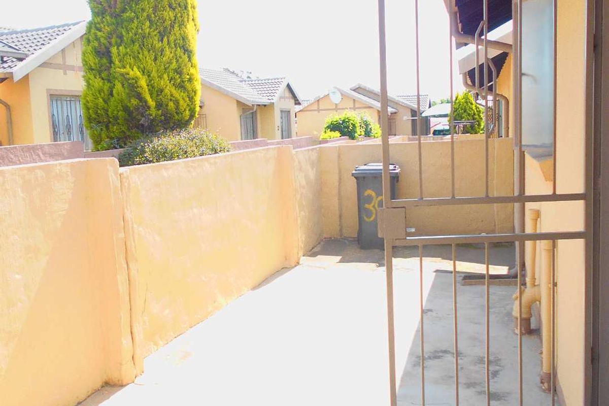 A paved rear courtyard area featuring a security gate and boundary wall, providing a functional outdoor space for the townhouse.