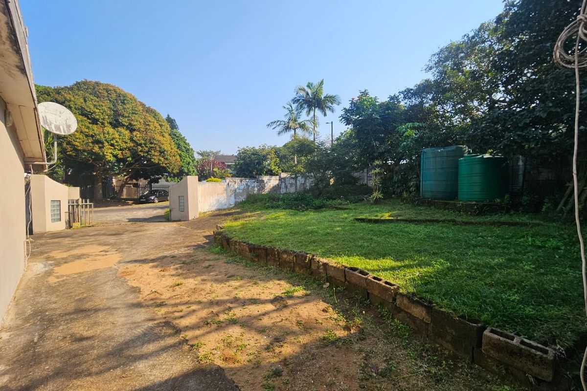 Rear exterior area featuring a concrete driveway, lawn with a low retaining wall, and water storage tanks against a boundary wall.