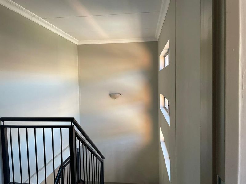 A bright stairwell featuring a modern metal balustrade, decorative wall sconce, and unique vertical slit windows providing natural light.