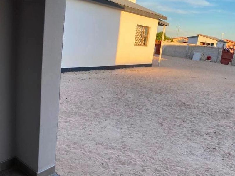 View from a tiled patio looking out over a large, unlandscaped sandy backyard enclosed by a perimeter wall.