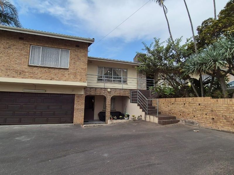 Front elevation of a multi-level brick house featuring a double garage, paved driveway, and an external staircase leading to an upper-level balcony.