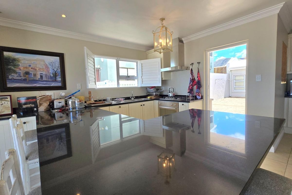 A functional kitchen featuring dark stone countertops, light-toned cabinetry, a built-in oven, gas hob, and an extractor fan, with direct access to the rear exterior.