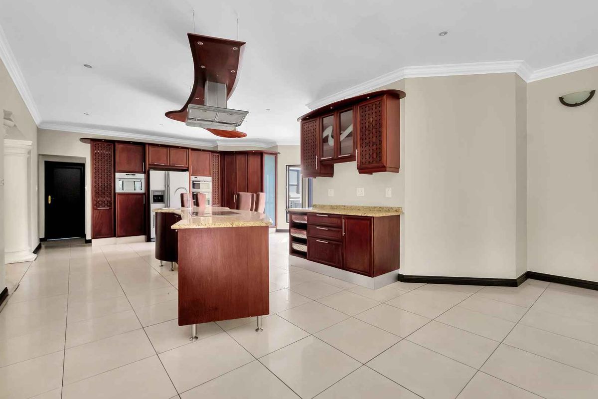 Spacious kitchen featuring cherry wood cabinetry, granite countertops, a central island, and a modern extractor fan, finished with neutral ceramic floor tiles.