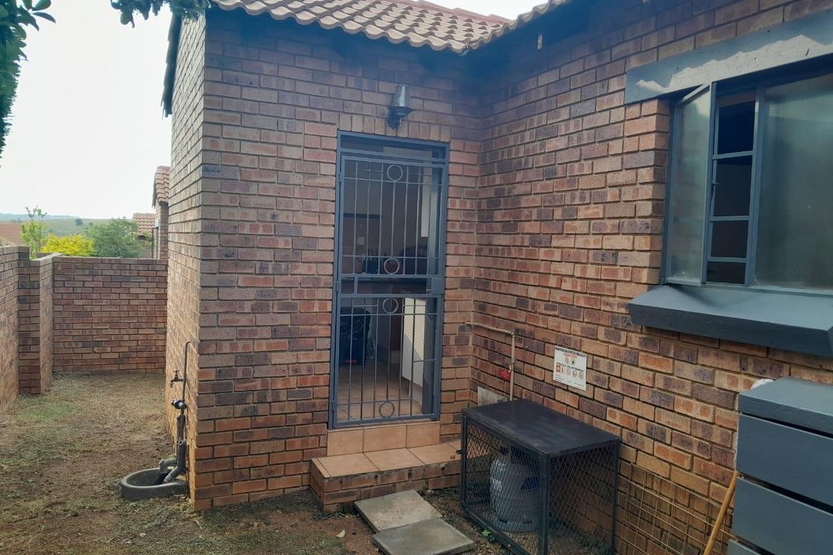 Rear exterior view of the townhouse featuring face-brick facade, security gate, outdoor tap, and a secure gas cylinder storage cage.