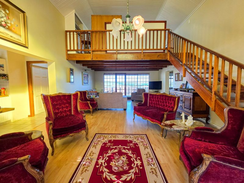 Spacious open-plan living area featuring a mezzanine level, wooden staircase, exposed ceiling beams, and large sliding doors leading to the exterior.