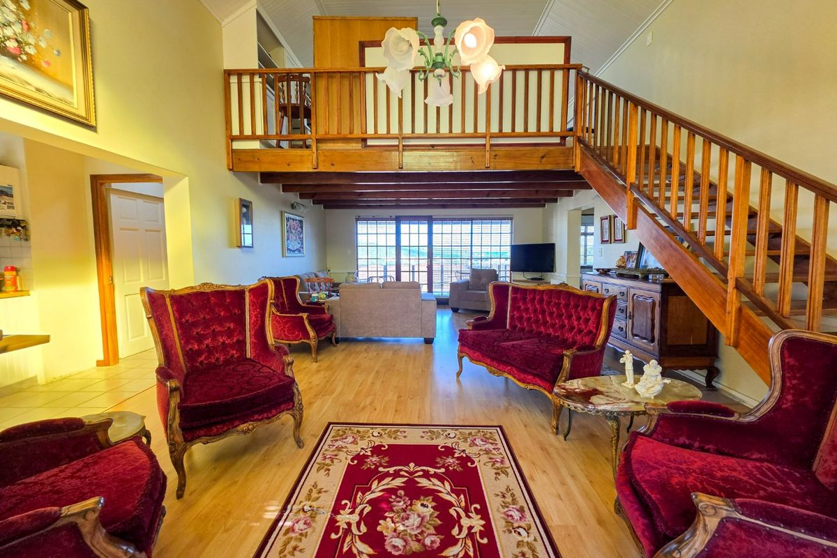 Spacious open-plan living area featuring a mezzanine level, wooden staircase, exposed ceiling beams, and large sliding doors leading to the exterior.