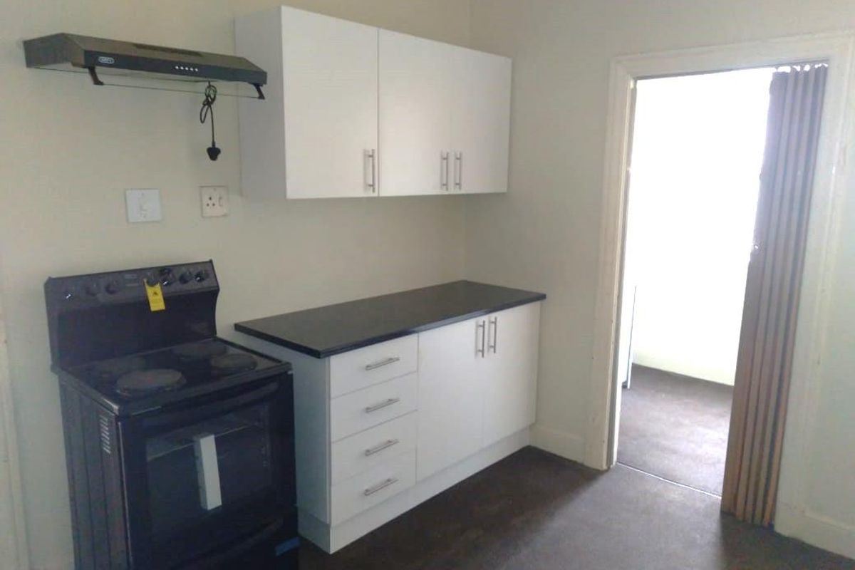 A functional kitchen area featuring white cabinetry, a black countertop, and a standalone electric stove with an overhead extractor fan.