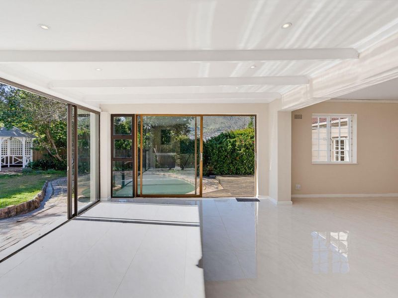 Spacious, light-filled living area featuring large sliding glass doors that open onto the garden, polished tiled floors, and exposed ceiling beams.