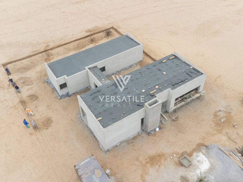 Aerial view of a residential property under construction, showing the concrete shell and flat roof structure on a sandy plot.