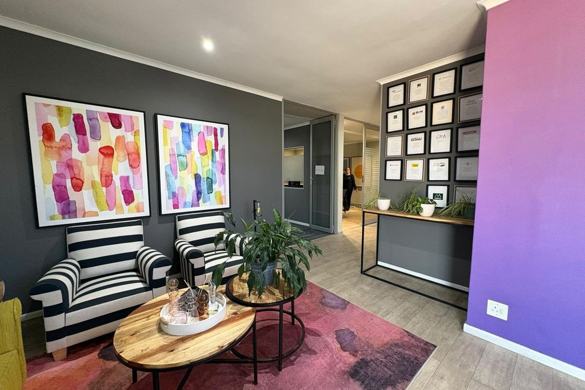 A modern office reception or waiting area featuring laminate flooring, recessed lighting, and a glass partition leading to further office space.