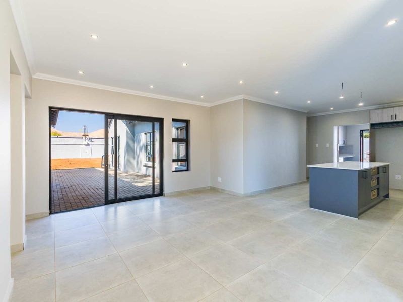 Spacious open-plan living and kitchen area featuring modern tiled flooring, recessed lighting, and large sliding doors leading to an outdoor patio.