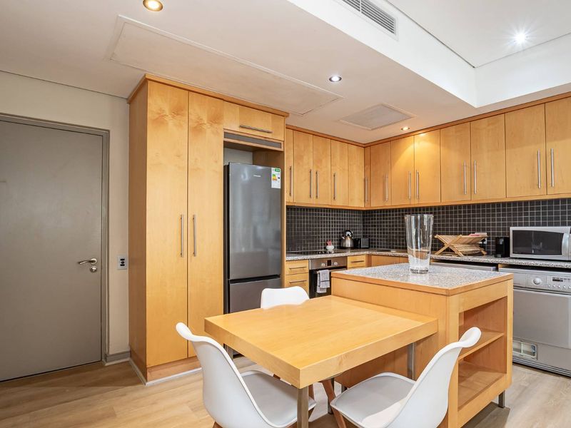 A functional kitchen featuring light wood cabinetry, stone countertops, a tiled backsplash, and a convenient built-in island with integrated dining space.