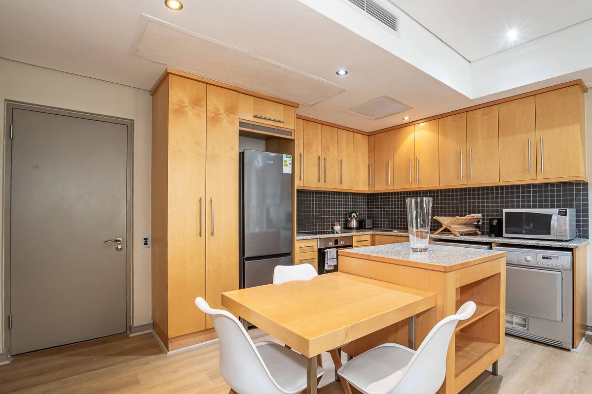 A functional kitchen featuring light wood cabinetry, stone countertops, a tiled backsplash, and a convenient built-in island with integrated dining space.