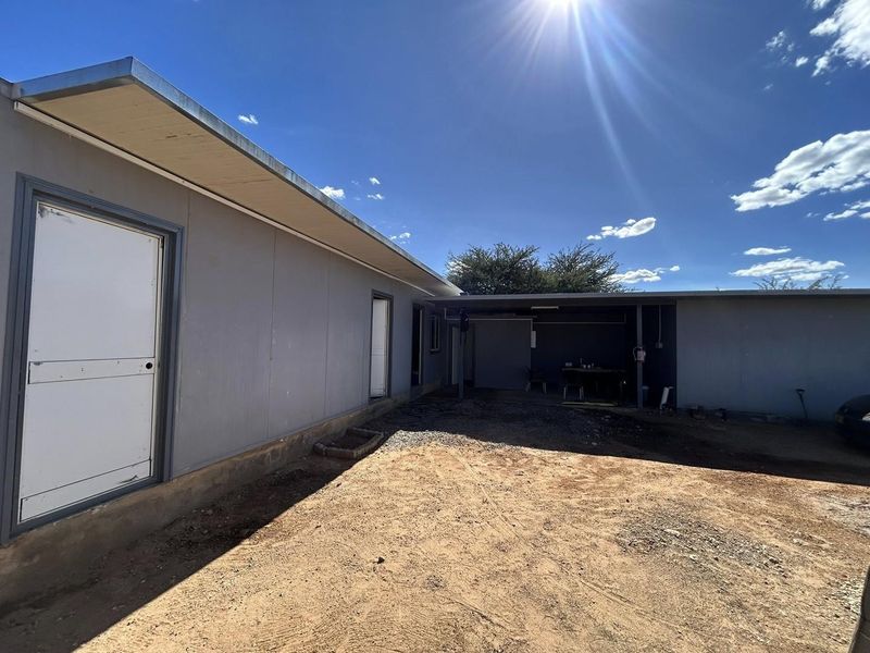 Rear exterior view of the property featuring a covered patio area and unpaved ground, offering potential for landscaping and outdoor improvement.