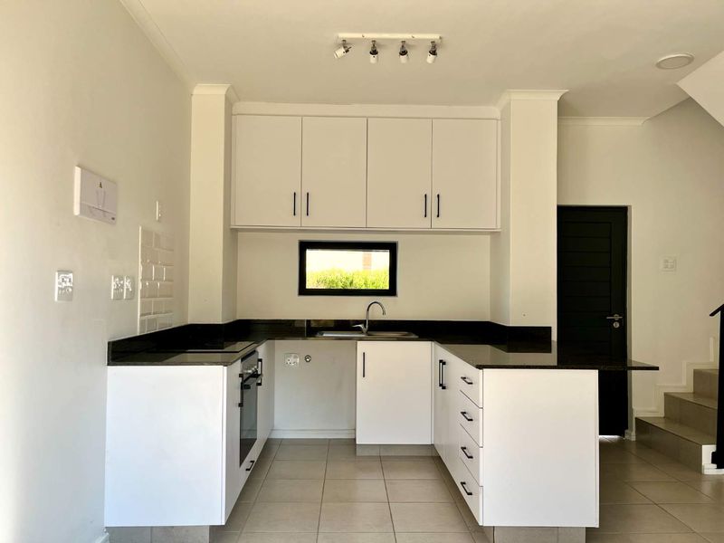 A clean, modern kitchen featuring white cabinetry, dark stone countertops, built-in oven, and tiled flooring in an open-plan layout.