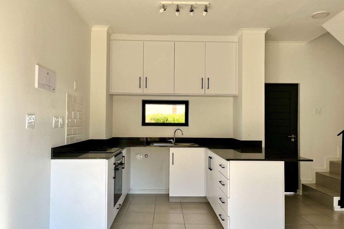 A clean, modern kitchen featuring white cabinetry, dark stone countertops, built-in oven, and tiled flooring in an open-plan layout.
