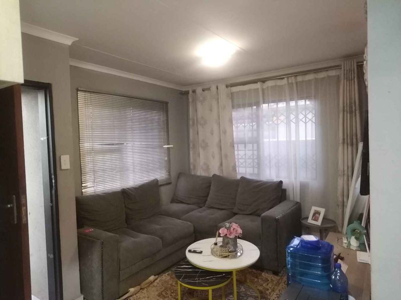 A comfortable living room featuring neutral wall tones, cove cornicing, and dual window treatments including venetian blinds and curtains.