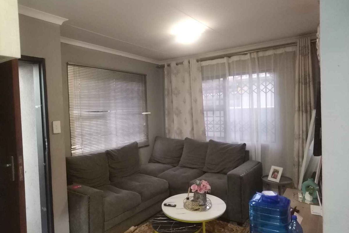 A comfortable living room featuring neutral wall tones, cove cornicing, and dual window treatments including venetian blinds and curtains.