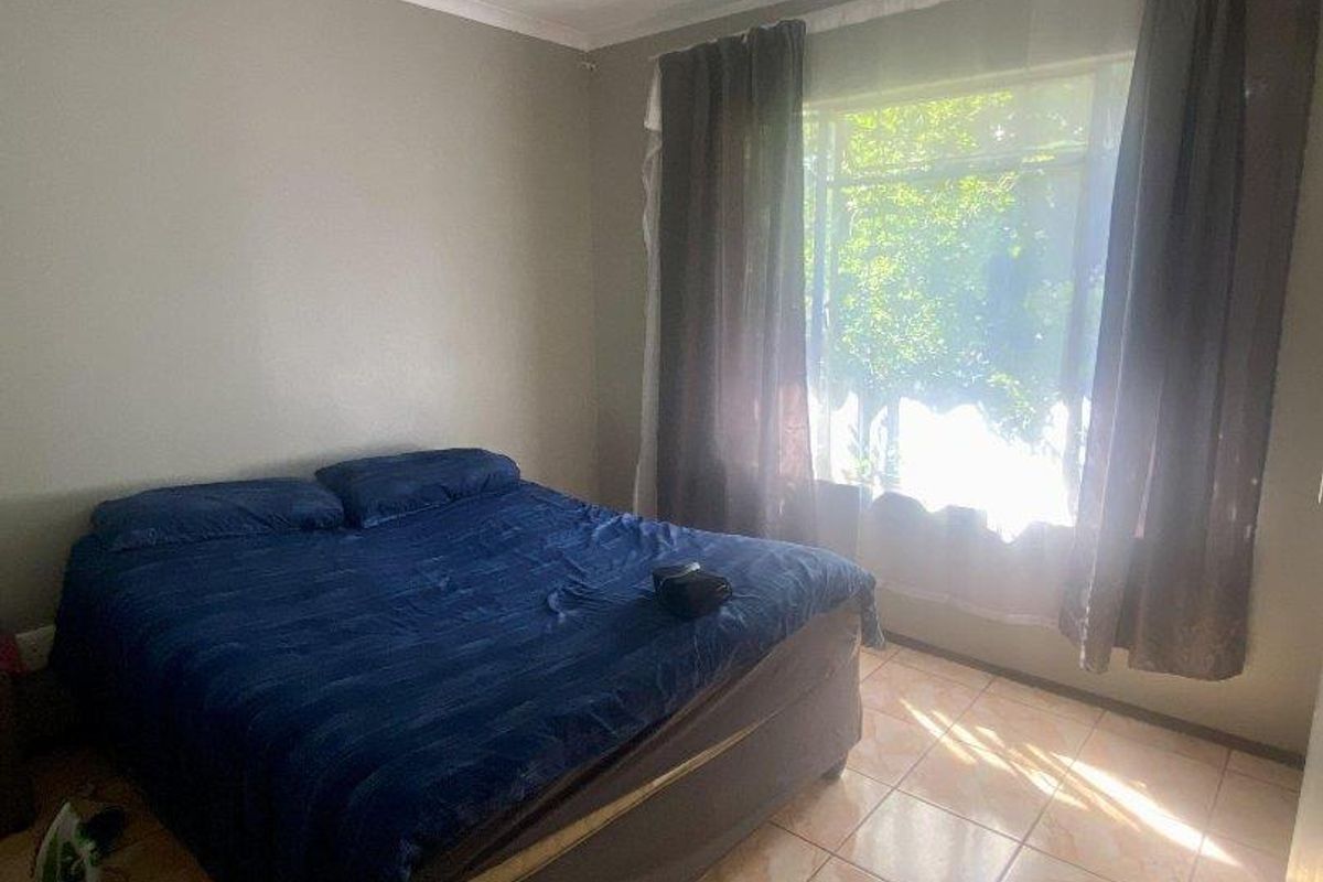 A bedroom featuring tiled flooring, a large window with curtains, and a ceiling-mounted light fixture.