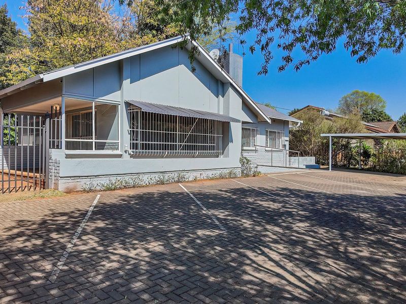 Front exterior view of the property featuring a paved driveway, carport, and secure perimeter fencing with security bars on windows.