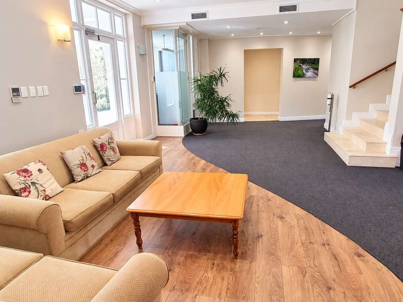 A bright and welcoming office reception area featuring a mix of wood-look flooring and carpet, with a staircase and glass-panelled entrance door.
